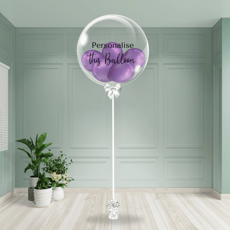 Elegant purple chrome balloons nestled inside a clear bubble balloon with customisable text, presented on a stylish stand, perfect for upscale events and brand celebrations.