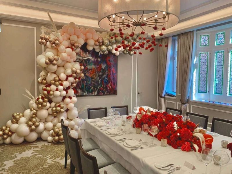 Luxury table setting with white, gold, and red balloon decor in an upscale dining space.