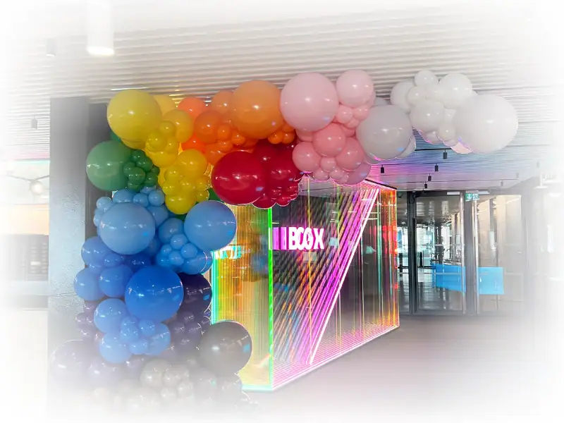 Pride rainbow balloon arch in corporate event space with neon backdrop
